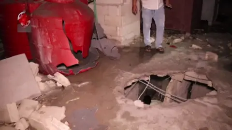 Al-Ikhbariya al-Suriyah TV Syrian state-run Al-Ikhbariya al-Suriyah TV footage shows a Syrian man standing next to a hole in the roof of a building reportedly hit in an Israeli strike in the Syrian port city of Tartous (9 September 2024)