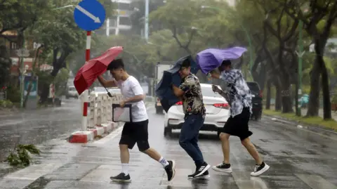 EPA People hold umbrellas as they cross a street under the rain in Hanoi, Vietnam, 7 September 2024